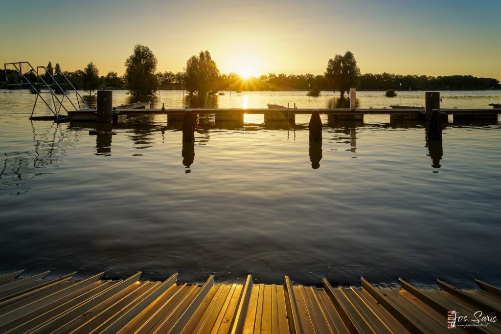 a dock over water with trees and a sunset