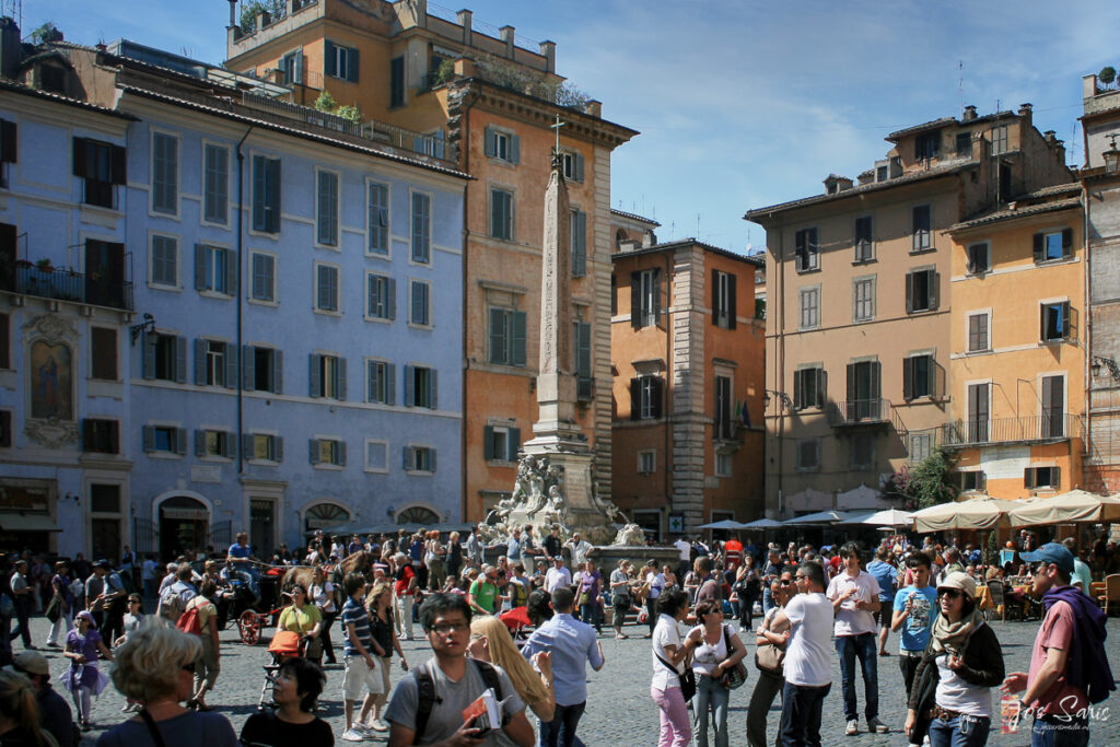 a group of people in a square with a tall monument in the background