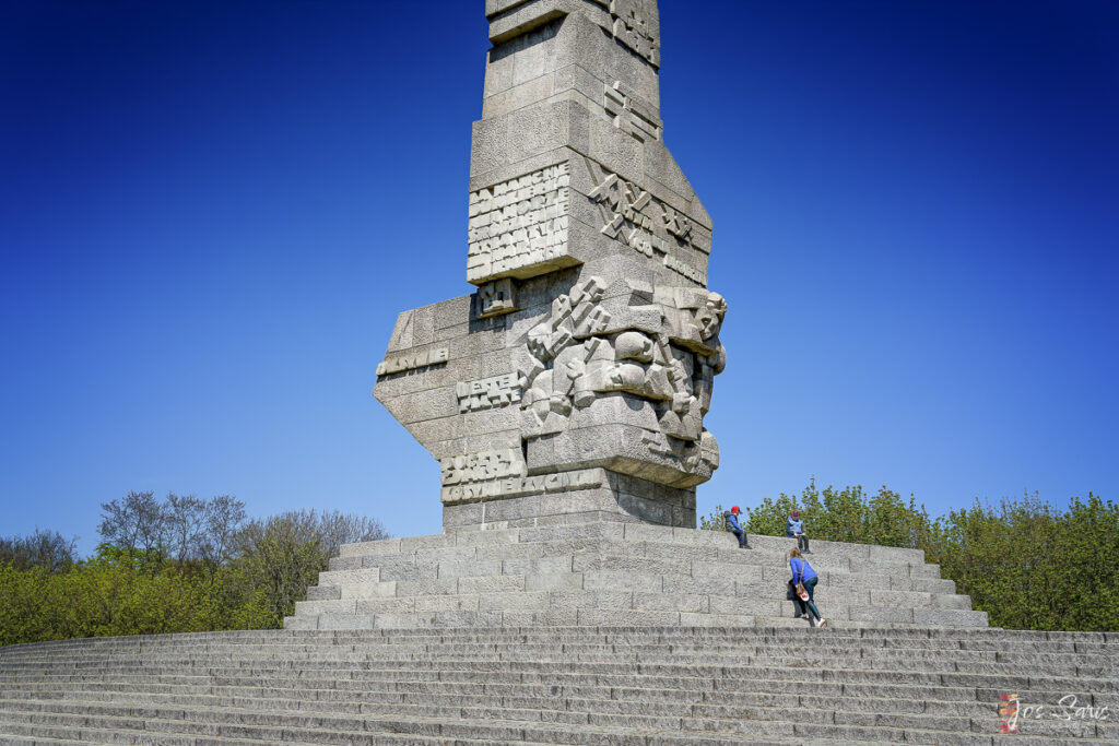 a stone statue with people on it with National Monument to the Forefathers in the background