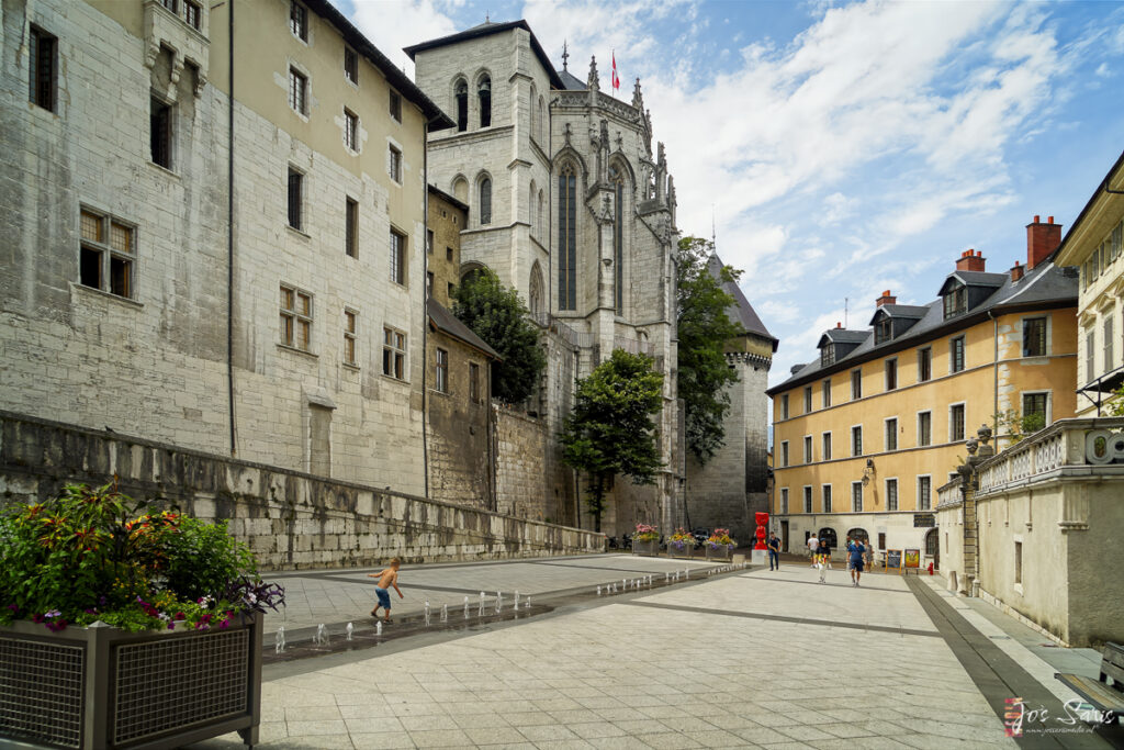 a stone building with a large tower and people walking in the street