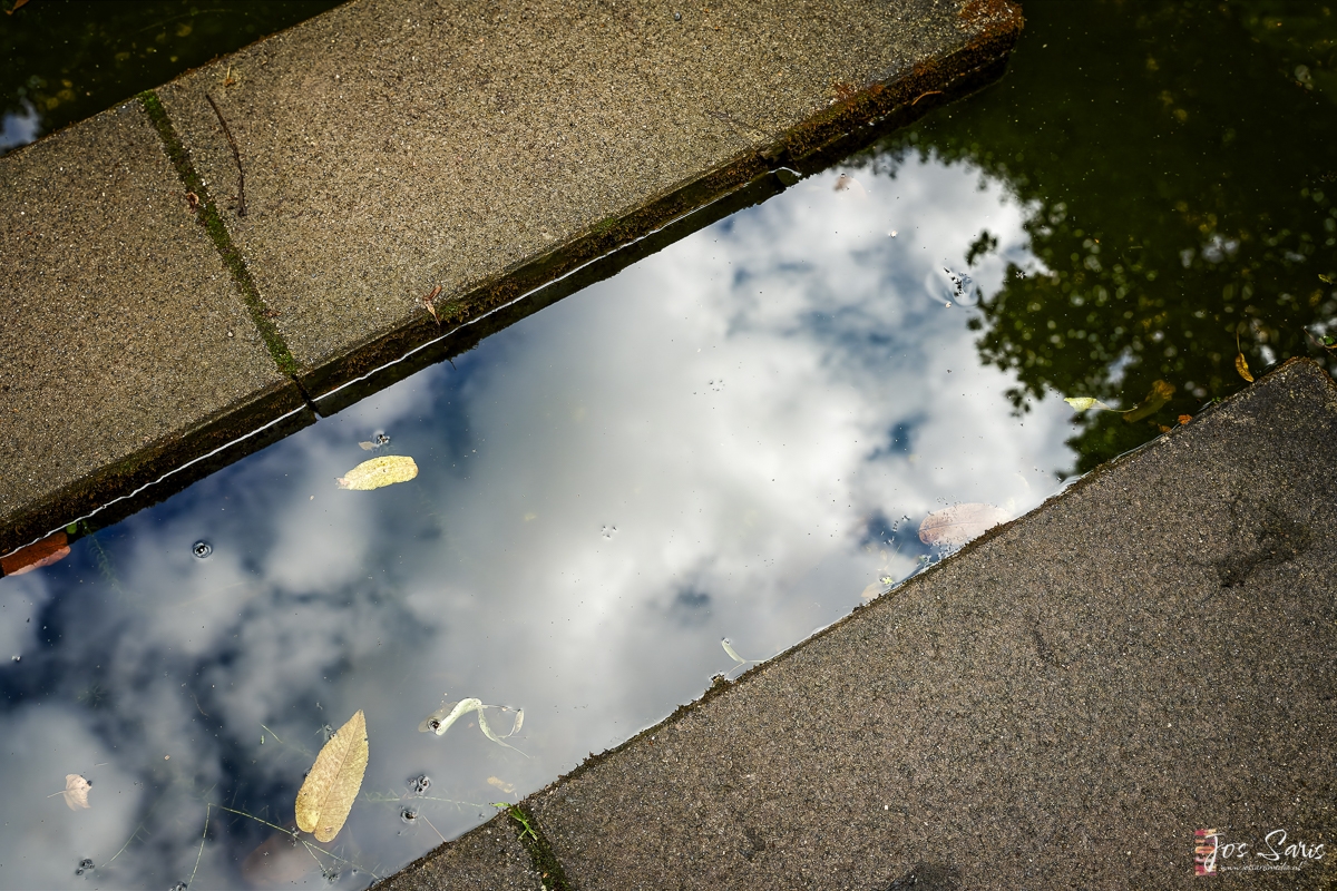 a puddle of water with clouds and sky reflected in it